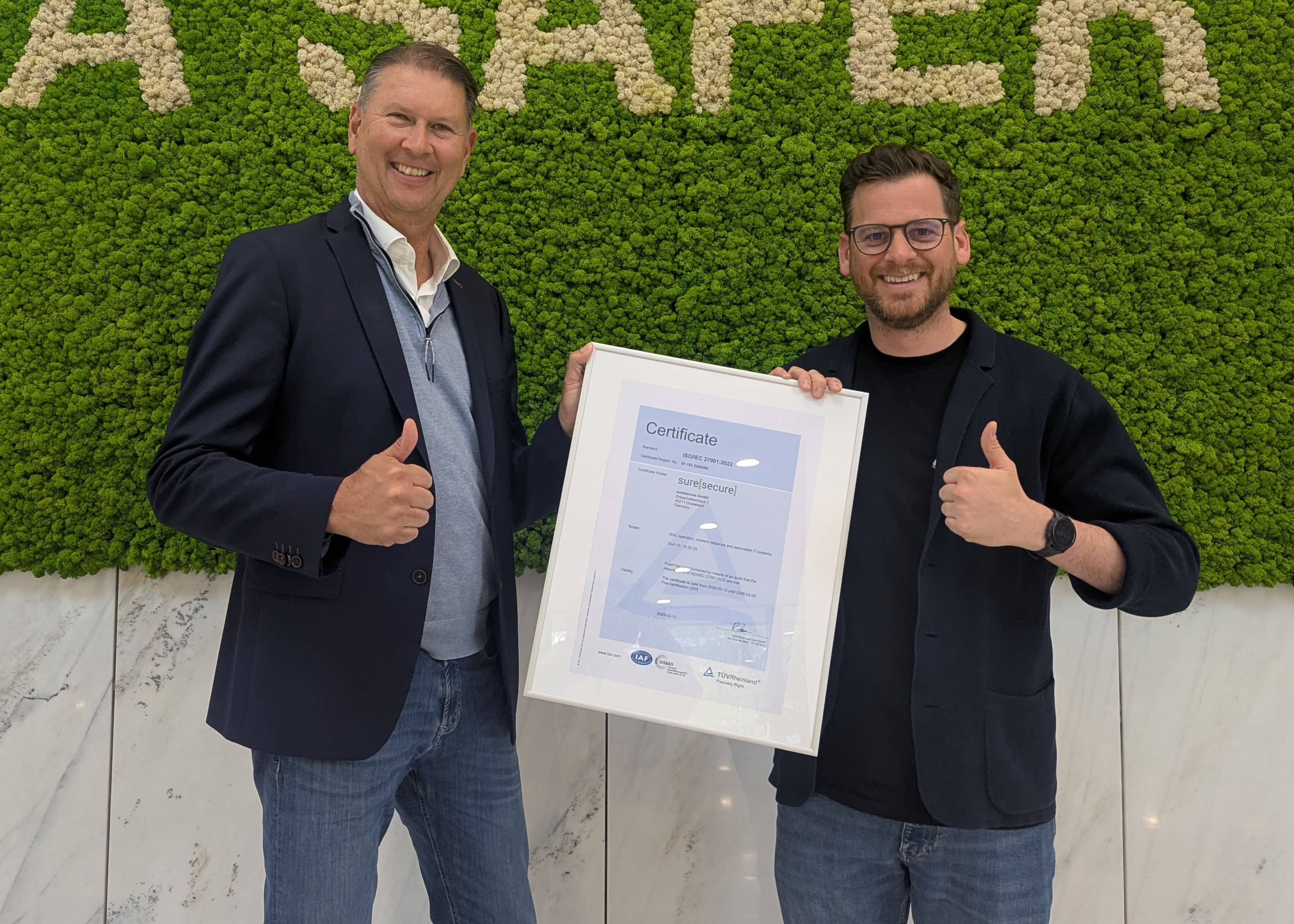 Michael Döhmen und ein Vertreter vom TÜV Rheinland halten das ISO Zertifikat der suresecure hoch.