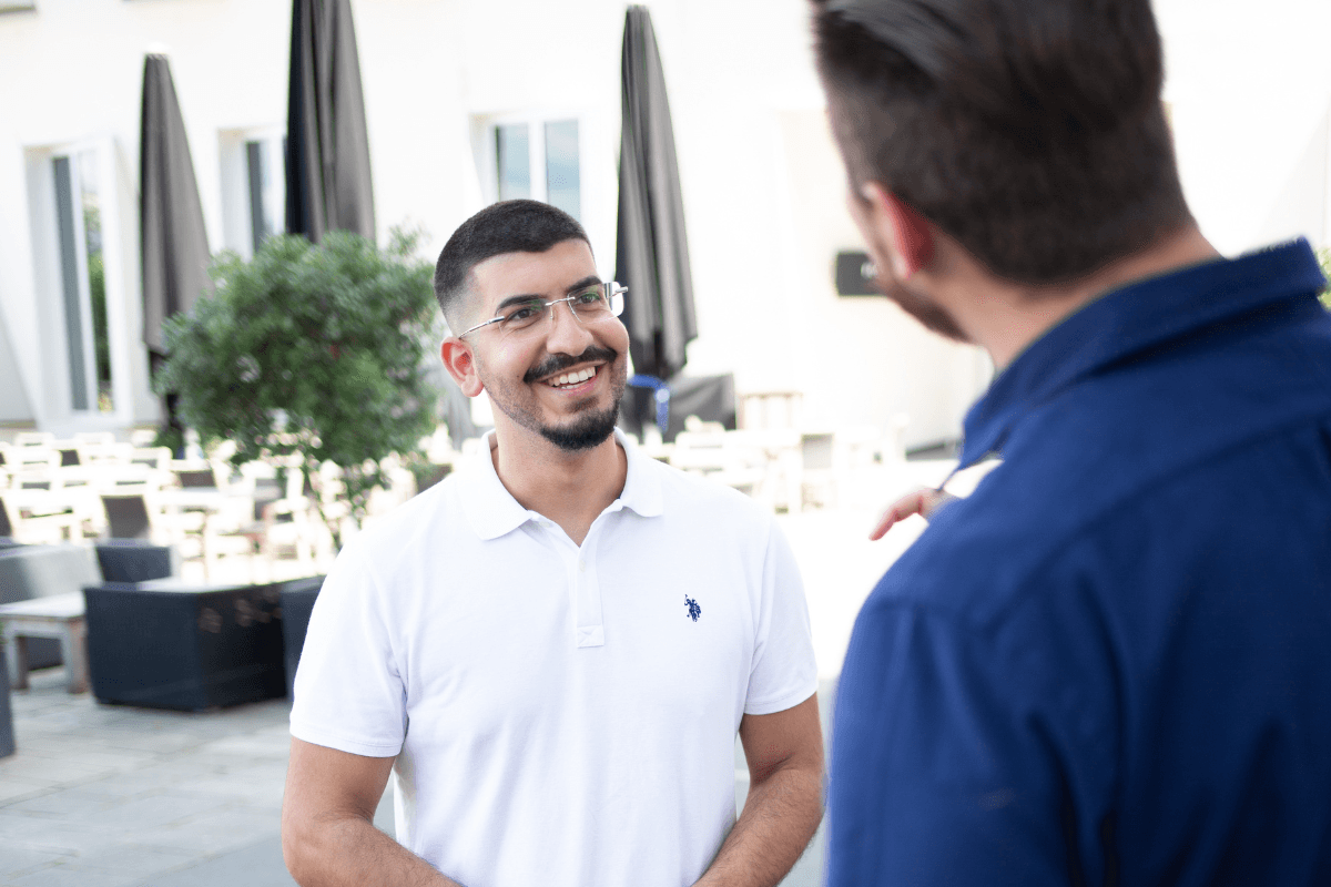 Zwei Geschäftspartner im Gespräch über IT-Sicherheitslösungen auf einer modernen Terrasse, Fokus auf vertrauensvolle Zusammenarbeit im Bereich Cybersecurity mit Cyberversicherung für Unternehmen.