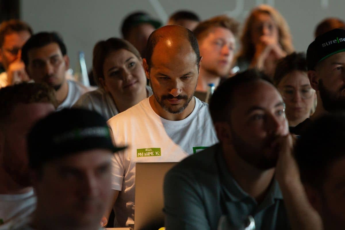 Teilnehmende einer IT-Konferenz oder Schulung sitzen aufmerksam im Publikum – Fokus auf einen Mann mit Laptop in einem Seminarraum.